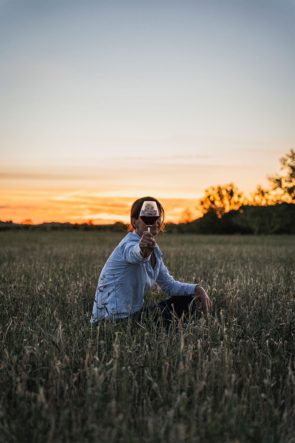 Photo portrait prise par le photographe professionnel Les insensés représentant une vigneronne Pays d'Oc IGP dans un champ avec un verre de vin